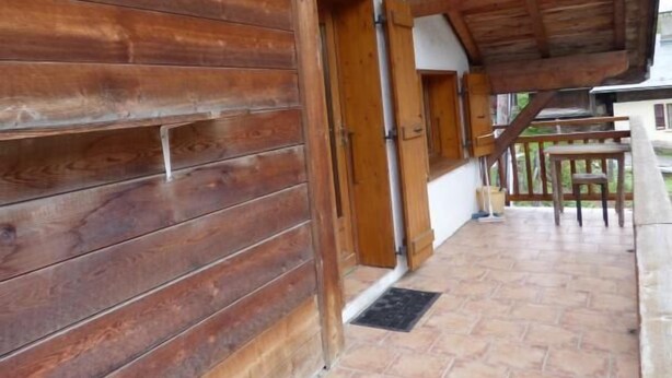 Una cabaña de madera con un porche cubierto, paredes de madera y suelo de baldosas.