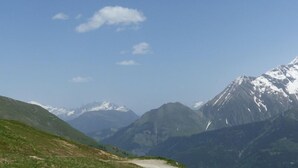 Paisaje montañoso con cielo despejado y un sendero de tierra que atraviesa un valle.