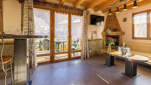 A rustic kitchen with wooden beams, a stone fireplace, and a large window overlooking a garden.