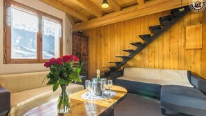 A cozy room with a wooden staircase, a sofa, a table with a vase of flowers, and a bottle of champagne.
