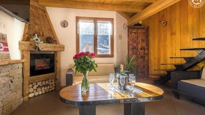 A cozy room with a stone fireplace, a wooden ceiling, and a dining table with wine glasses.