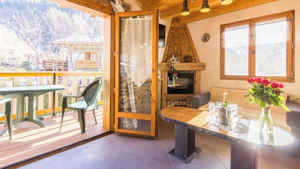 A cozy room with a wooden ceiling, a fireplace, a dining table with chairs, and a view of the mountains.