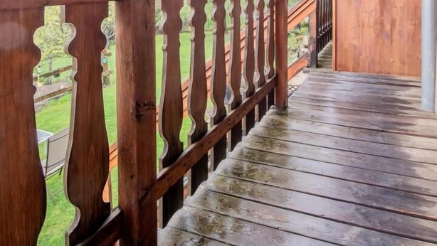 A wooden deck with a railing, leading to a covered area with a view of a forested hillside. - LA CASCADE - SAINT PANCRACE (SAINT PANCRACE)
