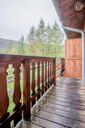 A wooden deck with a railing, leading to a covered area with a view of a forested hillside. - LA CASCADE - SAINT PANCRACE (SAINT PANCRACE)