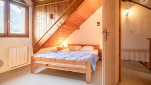 A bedroom with a sloped ceiling, wooden bed frame, and a window with a view of the outdoors. - LA CASCADE - SAINT PANCRACE (SAINT PANCRACE)