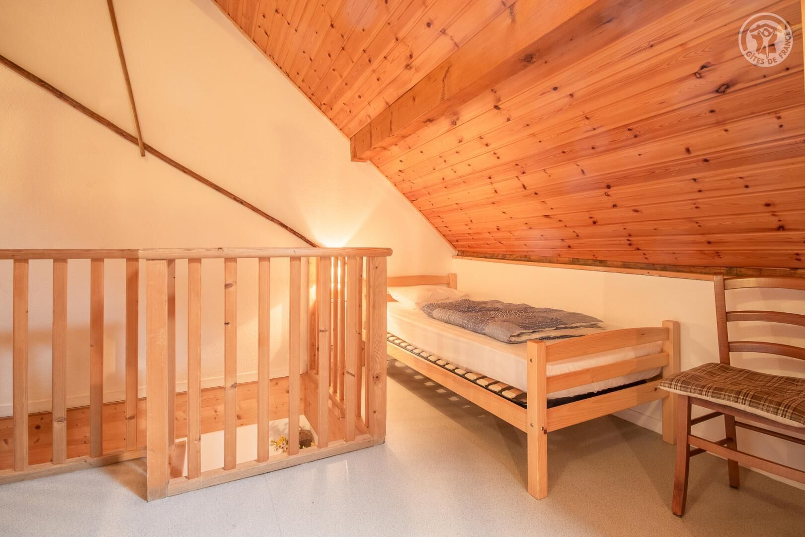 A wooden loft bedroom with a bunk bed and a chair.