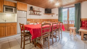 A cozy kitchen with wooden cabinets, a dining table with chairs, a microwave, and a refrigerator. - LA CASCADE - SAINT PANCRACE (SAINT PANCRACE)