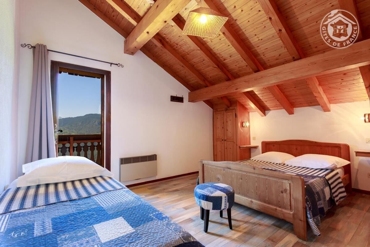 Une chambre à coucher avec un cadre en bois, comprenant un lit, un banc et donnant sur l’extérieur.