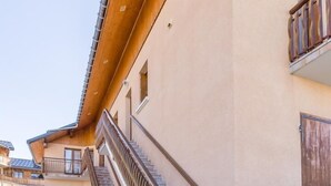 Un edificio con fachada de madera, una escalera y una entrada protegida por una reja.