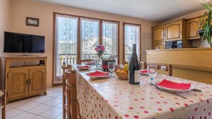 Un comedor con una mesa preparada para dos personas, una botella de vino y una cesta de fruta.