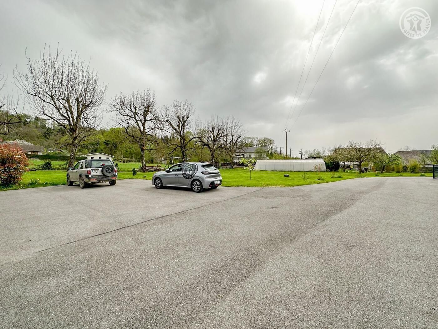 Un'area di parcheggio con due auto, una serra e cielo nuvoloso.