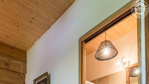 A wooden-paneled room with a blue chair, a red towel on the door, and a red rug leading to a bathroom with a mirror and sink. - LOU MANSOU - LA MOTTE EN BAUGES (LA MOTTE EN BAUGES)