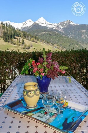 Une table avec un vase de fleurs, une carafe et des verres, le tout placé devant un paysage de montagne.