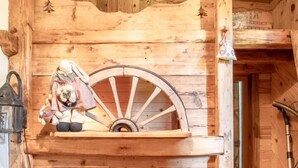 Ein Holzblockhaus-Interieur mit einem Bett, einer Holzwand mit einem Wagenrad und einem kleinen Regal mit Figuren.