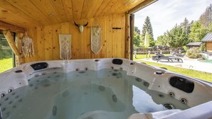 Eine Holzhütte mit Whirlpool und Blick auf den umliegenden Wald.