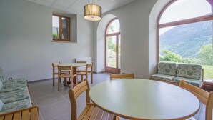 A dining area with a round table and chairs, large arched windows, and a view of a mountainous landscape.