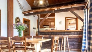 Ein rustikales Interieur mit Holzbalken, einer Essecke mit Stühlen, einer Küche mit Holzausbau und einer Hängeleuchte.