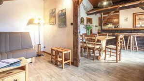 Ein gemütliches Wohnzimmer mit einer Couch, Holzstühlen, einem Esstisch und einer Küchenzeile mit Holzbalken und einer hängenden Leuchte.
