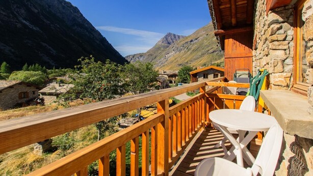 Un balcón de madera con una mesa y sillas, con vistas a un paisaje montañoso y edificios de piedra tradicionales.
