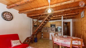 Una sala de estar acogedora con un sofá rojo, una mesa de comedor de madera y una escalera que lleva a una cocina.