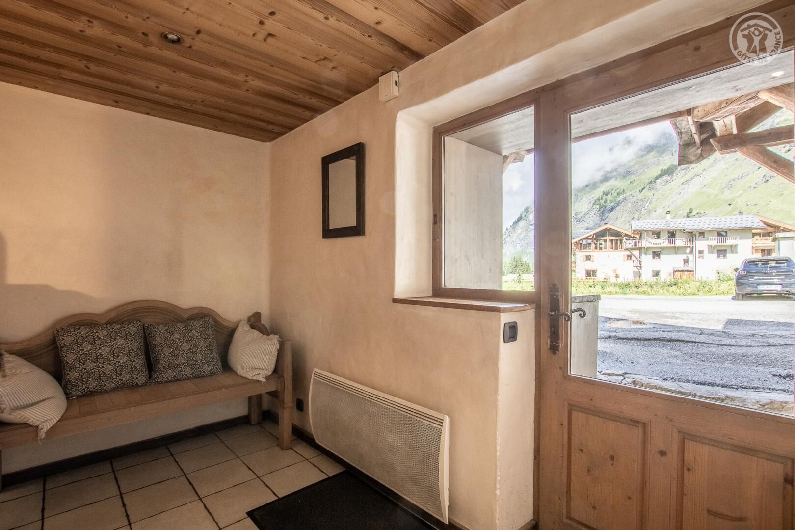 Een houten interieur met een bank, een radiator en een deur met uitzicht op de bergen.