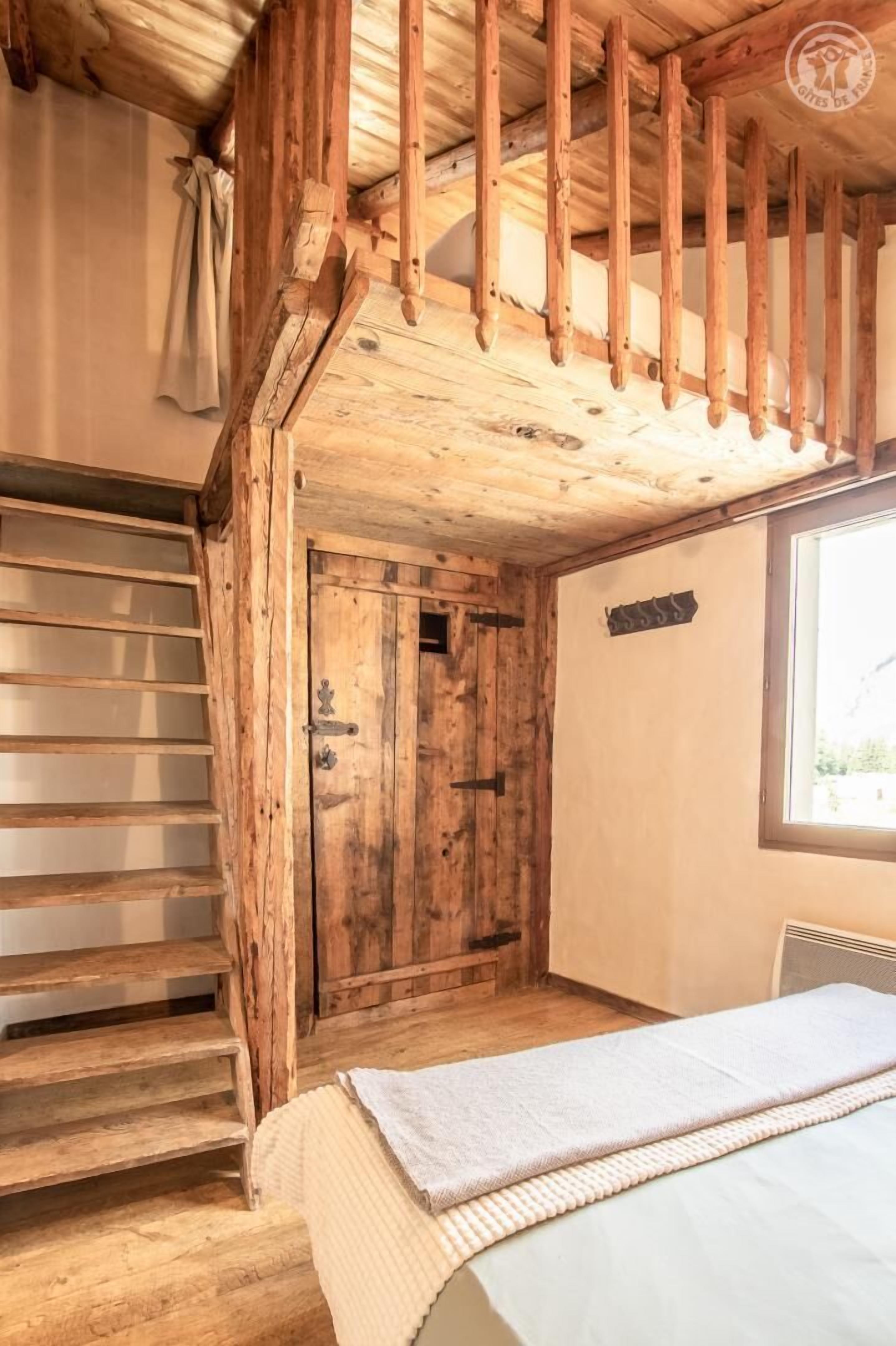 A rustic wooden room with a bed, a wooden staircase, and a door.