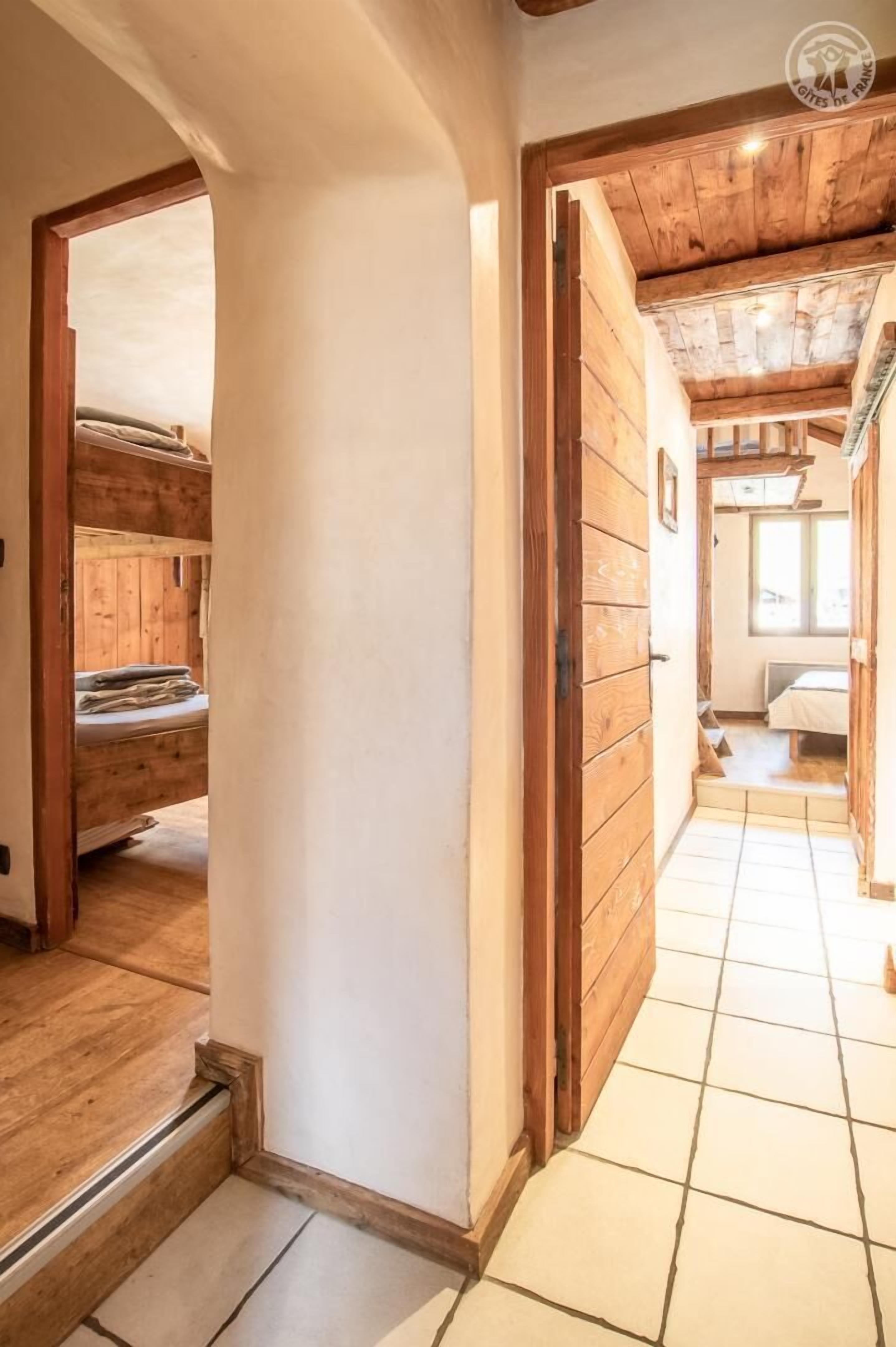 A hallway with wooden walls and a tiled floor, leading to a bedroom with a bed and a window.