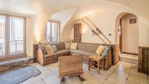 Una habitación acogedora con un banco de madera, un sofá y una mesa. Hay ventanas y una escalera que sube a otro nivel.