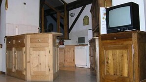 A kitchen with wooden cabinets, a refrigerator, and a television on a wooden stand.