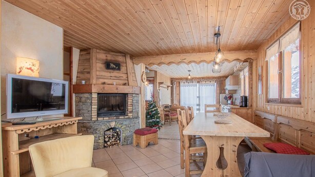 L’intérieur d’un chalet en bois chaleureux et accueillant, avec une cheminée, un coin repas et un téléviseur.