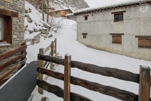 A stone building with wooden shutters, a wooden fence, and a metal staircase leading up to a door. - L'AIGLE - BONNEVAL SUR ARC (BONNEVAL SUR ARC)