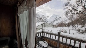 Un balcon en bois offrant une vue sur une montagne enneigée et une petite maison.