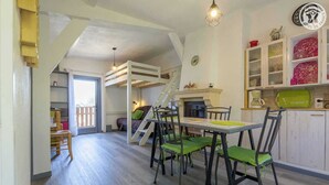 Una habitació acollidora amb un llit doble superior, una taula de dinar amb cadires i una zona de cuina amb armaris i una cafetera.