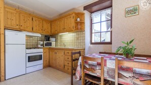 Une cuisine avec des meubles de rangement en bois, un réfrigérateur, une cuisinière, un four à micro-ondes et une table à manger recouverte d’une nappe matelassée.