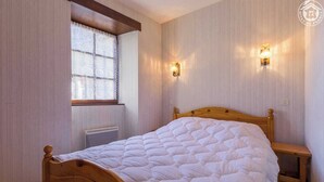 Une chambre à coucher avec un lit en bois, une fenêtre ornée de rideaux en dentelle et deux appliques murales.