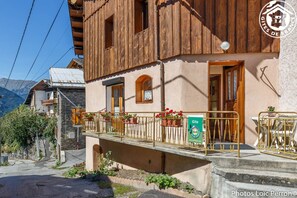 A rustic chalet with a balcony, stone walls, and a mountain backdrop.