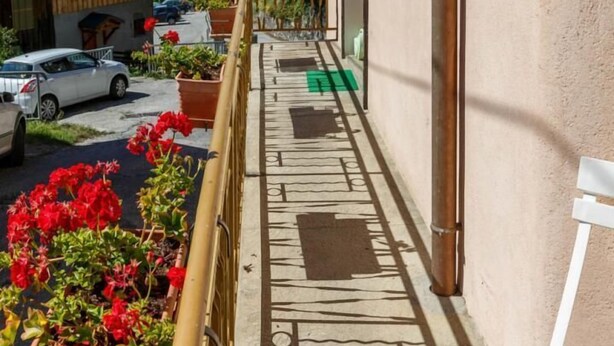 A narrow balcony with a view of a mountain, wooden buildings, and parked cars.