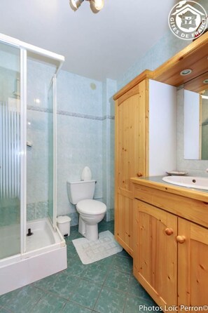 A bathroom with a glass-enclosed shower, a white toilet, and wooden cabinetry.