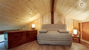 A cozy attic bedroom with a large bed, wooden walls, and a sloped ceiling. - LE RIEU - CHAMPAGNEUX (CHAMPAGNEUX)