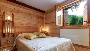 A wooden room with a bed, a window, and a wall-mounted light fixture. - LE RIEU - CHAMPAGNEUX (CHAMPAGNEUX)
