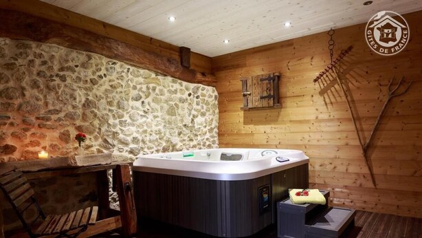A wooden cabin with a stone wall, a hot tub, a wooden bench, and a rustic interior. - LE RIEU - CHAMPAGNEUX (CHAMPAGNEUX)