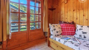 Een houten kamer met een groot raam, een houten bed met beddengoed met een patroon, en een houten wand.