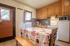A small kitchen with wooden cabinets, a stove, a microwave, and a table with a red and white tablecloth.
