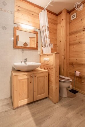 Compact bathroom with a wooden vanity, white sink, and mirror.