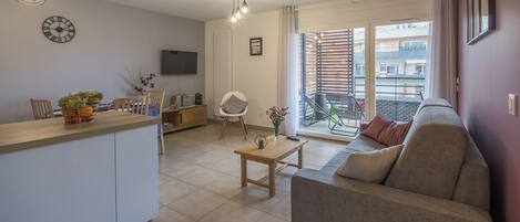 A modern apartment with a kitchen, dining area, and living room. It features a balcony with a view of the city.