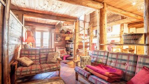 A cozy log cabin interior with plaid furniture, a fireplace, and a rustic wooden ceiling.