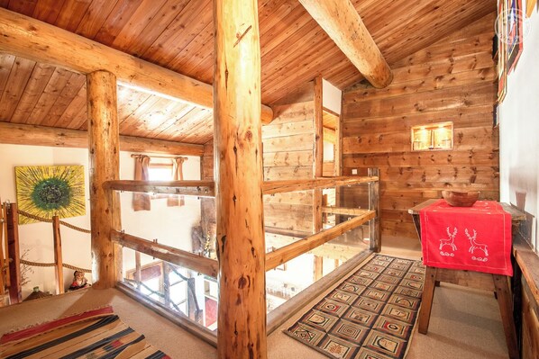A wooden cabin interior with a glass railing, a red tablecloth, and a patterned rug.