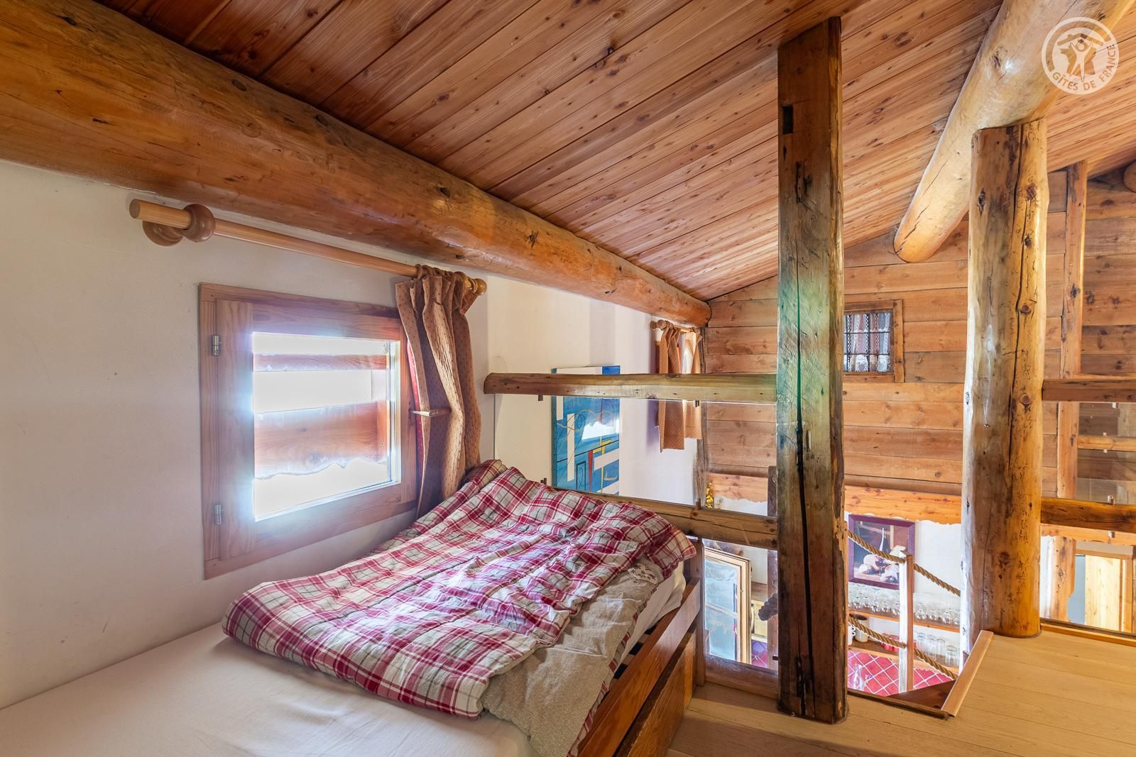 Habitación de cabaña de madera con literas, una ventana con cortinas y vistas al exterior.