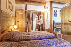 A wooden room with a bed, a nightstand, a lamp, and a window with a view.