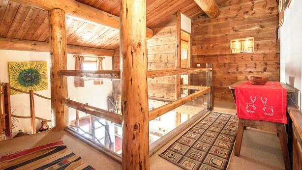 A wooden cabin interior with a glass railing, a red tablecloth with reindeer, and a patterned rug.